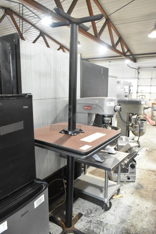 2 wood pattern bar height tables on black metal bases, shown in a storage area, industrial setting.