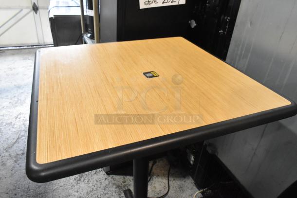Bar-height table with wood pattern top and black metal base. Good condition. Auction tag visible on the surface.