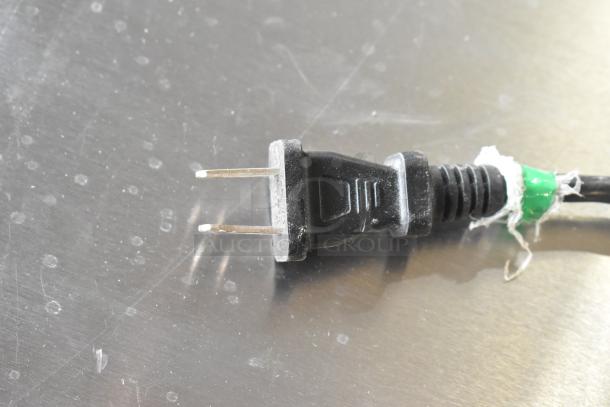 Black 2-prong power plug on a cord, resting on a metallic surface.