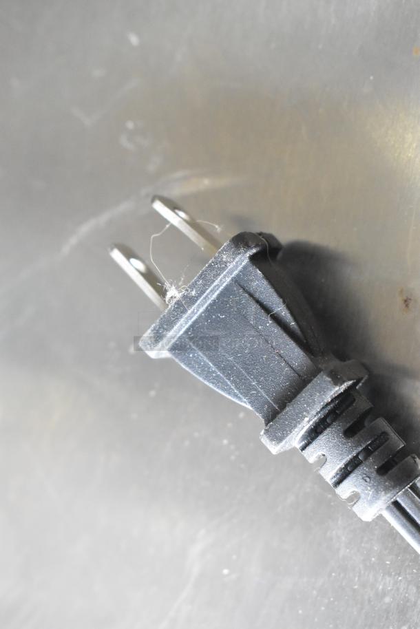 Black power plug for Singer countertop sewing machine, 120 volts, shown on a metal surface.
