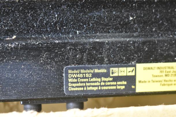 DeWalt DW451S2 Wide Crown Lathing Stapler label, showing model details and safety icons with dust on black surface.