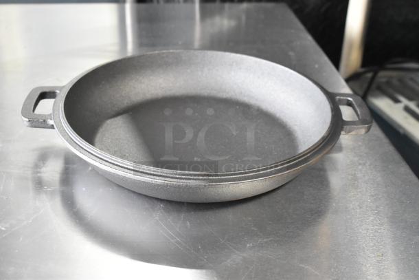 Cast iron skillet with dual handles on a metal surface, in good condition, part of a box set of pots and skillets.