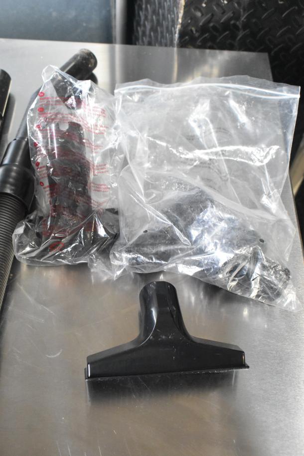 Oreck XL BB880-AD vacuum cleaner accessories, shown with hoses and attachments in plastic bags on a metallic surface.