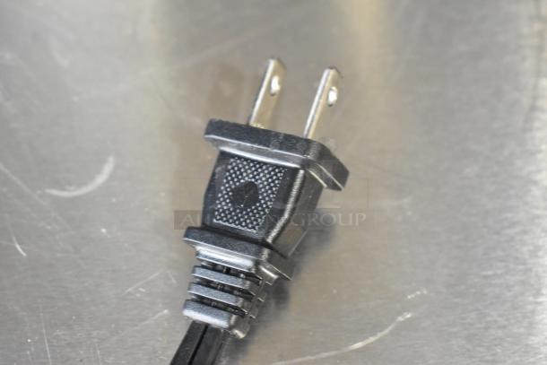 A close-up of a black electrical plug belonging to a Nespresso SA coffee machine.