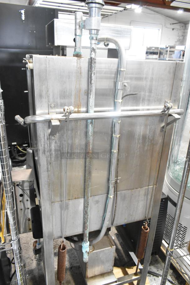 Jackson stainless steel commercial pass-through dishwasher, vertical orientation, visible piping, industrial setting, used condition.