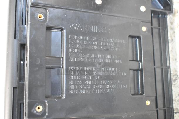 Close-up of the back of a flavor dispenser showing safety warnings against fire, electric shock, and liquid immersion.