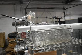 Brand new metal fry basket on a shelf, featuring a sturdy mesh design and black handle. Minor scratches and dents visible.