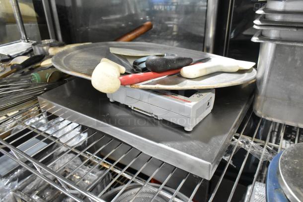 Assorted kitchen items including stainless steel drop-in bins, utensils, and various tools on metal shelving.