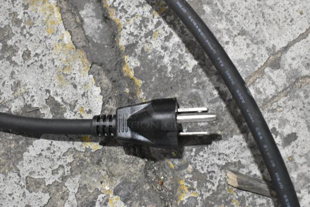 Black power cord with a three-prong plug lying on a concrete surface. Cord has visible text specifications.
