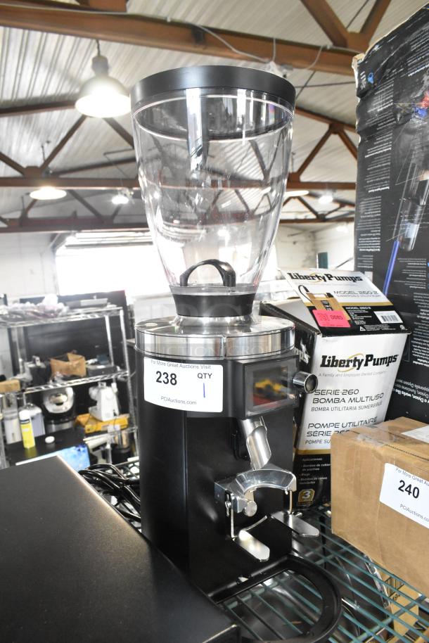 Alt text: Mahlkonig E65T black espresso grinder, 2.6 lb capacity, 120V, shows scratches, label indicates new condition.
