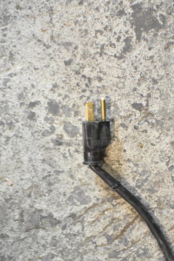 Close-up image of a black electric power cord plug lying on a textured concrete surface.