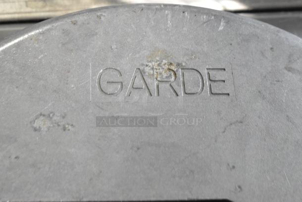Garde brand marking on metal surface with visible scratches and discoloration. Auction items include vegetable slicers and metal collar.