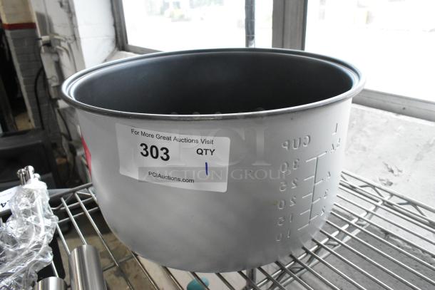 Brand new rice warmer insert with visible scratch and dent marks, numbered "303" from PCAAuctions.com, on metal shelf.