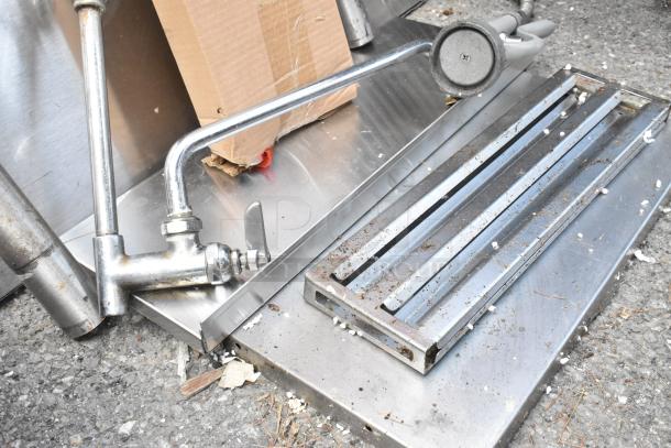 Lot of various metal pieces and legs, including a tap and steel grate. Visible wear, suitable for scrap or repurpose.