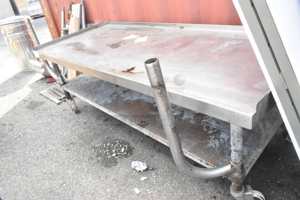 Stainless steel equipment stand with under shelf on commercial casters, shows signs of wear and surface rust.