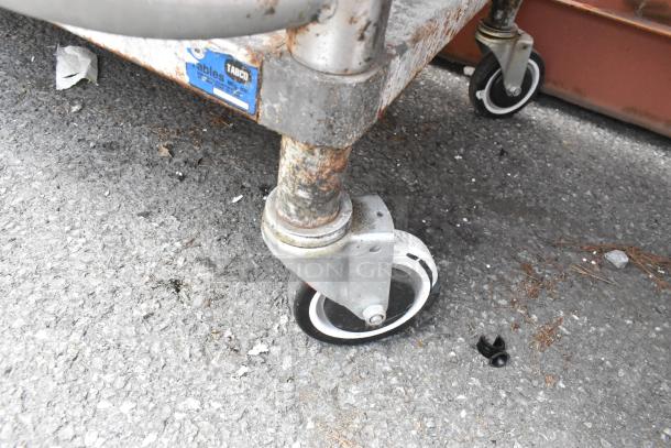 Stainless steel equipment stand with under shelf, commercial casters, visible wear, and a label with "Tabco" brand.