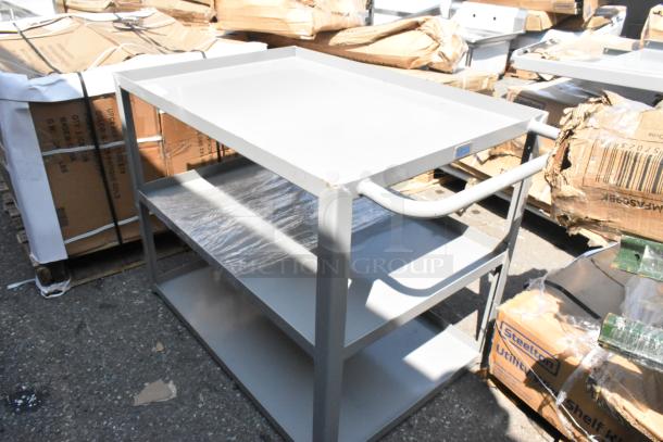 Gray metal 3-tier cart, brand new with scratches and dents, features sturdy shelves and a handle for mobility.
