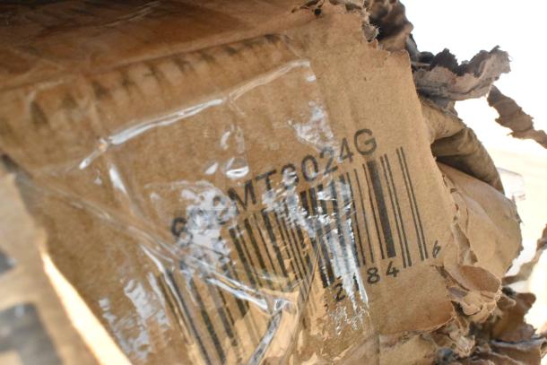 Cardboard box with visible barcode and code "608MT8024G," containing mixed new items like an umbrella and stainless steel mixer table.