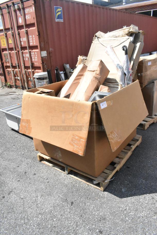 Cardboard box with 14 new scratch and dent items, including grab bar and anti-fatigue mat, on pallet outdoors.