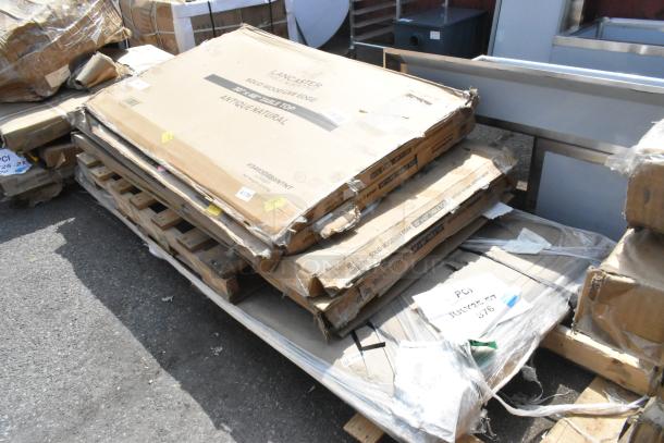 Pile of packaged items including Lancaster solid wood tabletops, labeled as scratch and dent, on pallets.