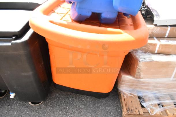 Three containers: a blue container on top, a large orange bin in front, and a black bus bin with wheels, stacked on a pallet.