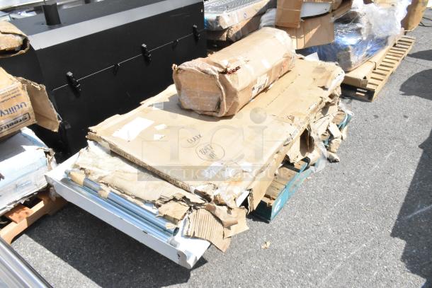 New scratch and dent items including a tabletop and stainless equipment stand in damaged packaging on a pallet.