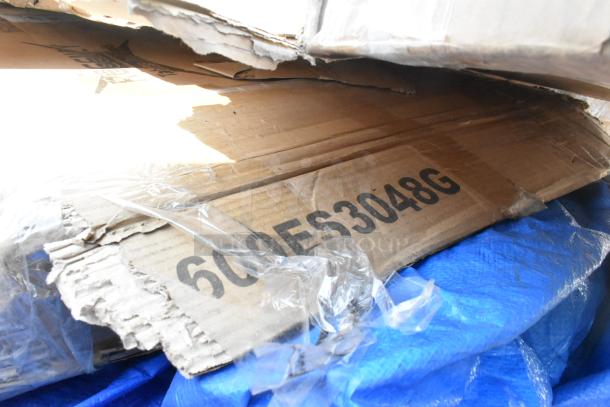 Cardboard packaging labeled "600ES3048G" with visible dents, containing six scratch and dent stainless tables and overshelf items.