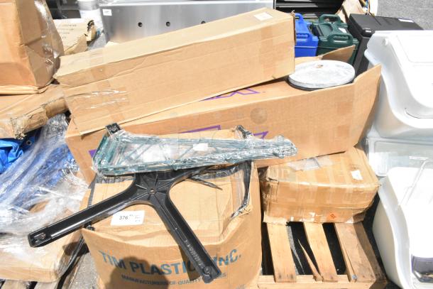 Assorted packaging containing seven new scratch and dent items, including cleaning brushes and trash cans, stacked on a pallet.