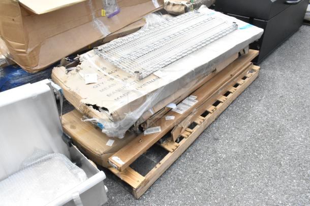 Eight new scratch and dent items, including stainless table, pan rack, and posts, on a pallet. Packaging shows wear.