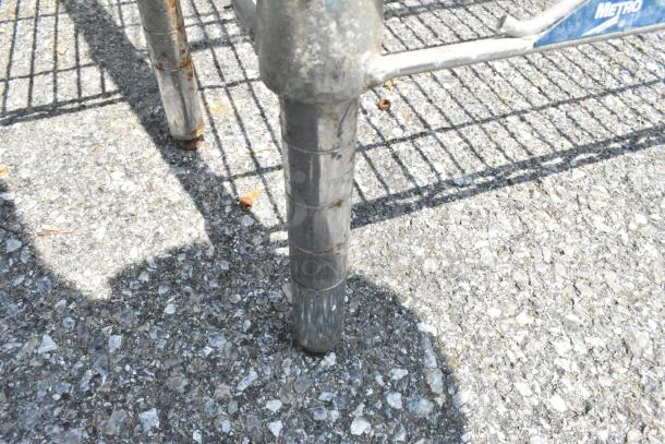 Metro chrome finish 4-tier wire shelving unit leg detail on pavement, visible wear. Buyer to dismantle for transport.