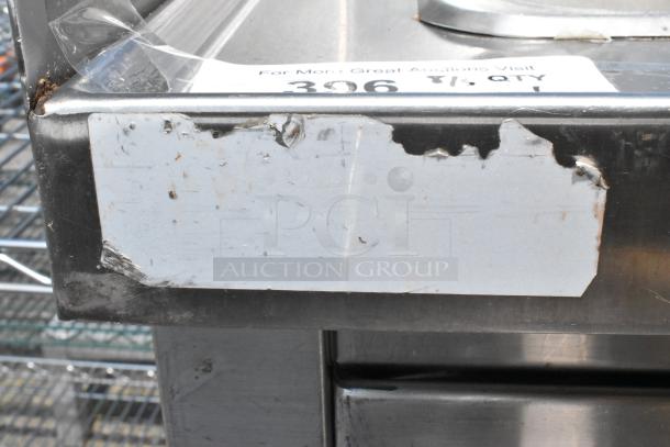 Stainless steel single bay sink with faucet, handles, and side splash guards. Item shows wear with visible scratches and labels.