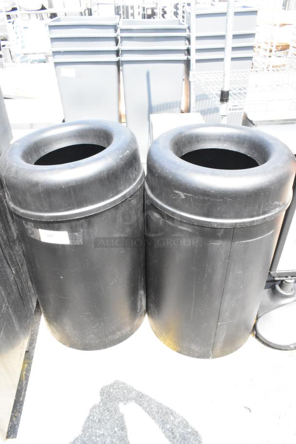Two black trash can shells in good condition, featuring cylindrical design and open tops. One has a visible label.