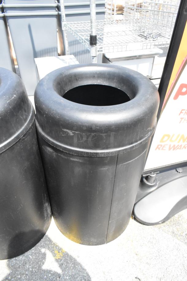 Two large black trash can shells, made of durable material, in used condition. Ideal for outdoor settings.