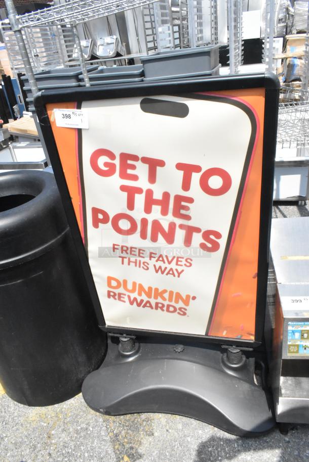 Black sidewalk sign advertising Dunkin' Rewards, features red and orange text. Sign is intact and positioned outdoors.