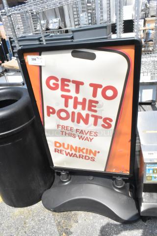Black sidewalk sign advertising Dunkin' Rewards, features red and orange text. Sign is intact and positioned outdoors.