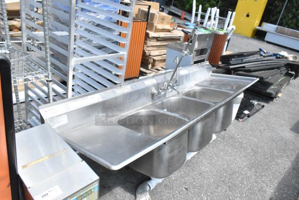 Eagle Stainless Steel 3 Bay Sink with dual drain boards and faucet handles. No legs. Signs of use, suitable for commercial kitchen.