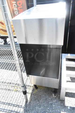 Stainless steel countertop dispenser stand with a sleek design, featuring sturdy black feet and a spacious compartment.
