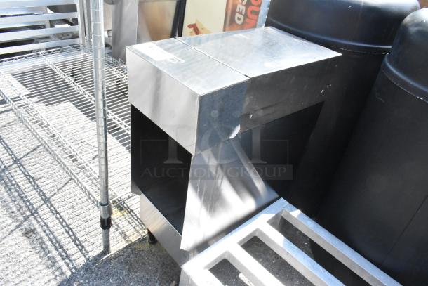 Stainless steel countertop dispenser stand with angular design, visible scuffs, robust construction; ideal for commercial use.
