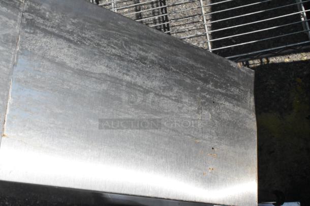 Stainless steel countertop dispenser stand with a brushed finish, minor surface wear, and circular rust spots.