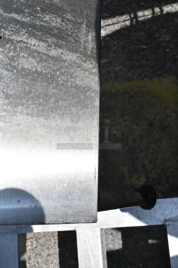 Stainless steel countertop dispenser stand with visible wear. Slight scratches and marks on surface, sturdy construction.