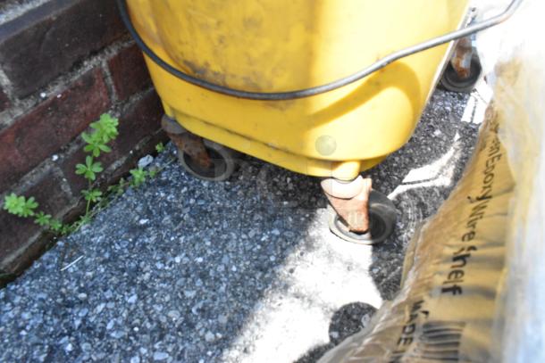 Yellow poly mop bucket with wringing attachment on commercial casters, used condition, visible wear on wheels.