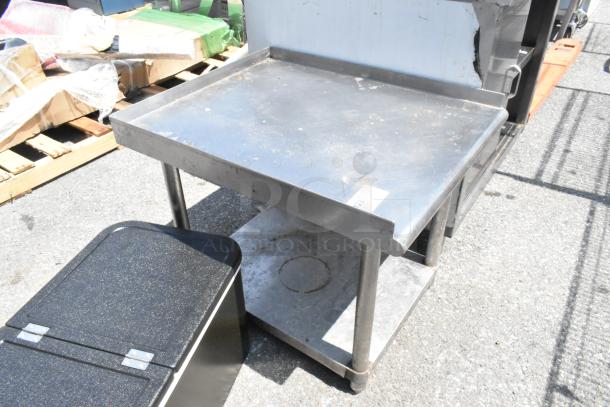 Stainless steel equipment stand with metal under shelf, showing signs of wear. Ideal for kitchen or industrial use.