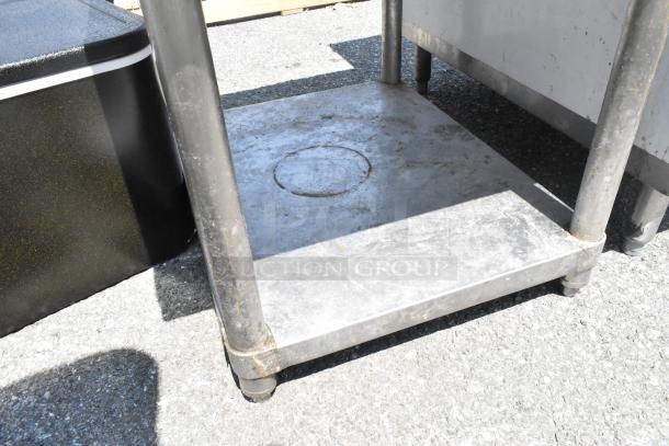 Stainless steel equipment stand with metal under shelf, showing signs of wear. Sturdy legs and clean finish. Ideal for kitchens.