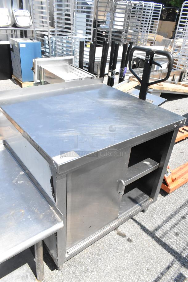 Stainless steel table with two under shelves and a door, showing minimal wear, ideal for storage and prep.