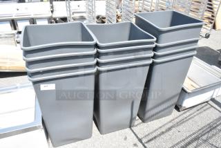 12 brand new gray poly trash cans with minor scratches visible. Stacked and ready for auction.