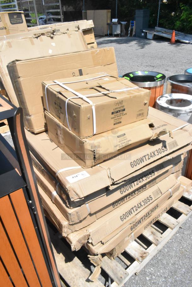 Boxes of brand new items including Regency stainless steel work tables and Lancaster cast iron table bases with visible model numbers.