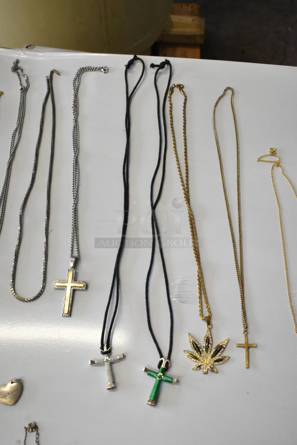 Lot of assorted jewelry featuring necklaces with cross and leaf pendants, earrings, and a heart-shaped ring, in mixed metals.