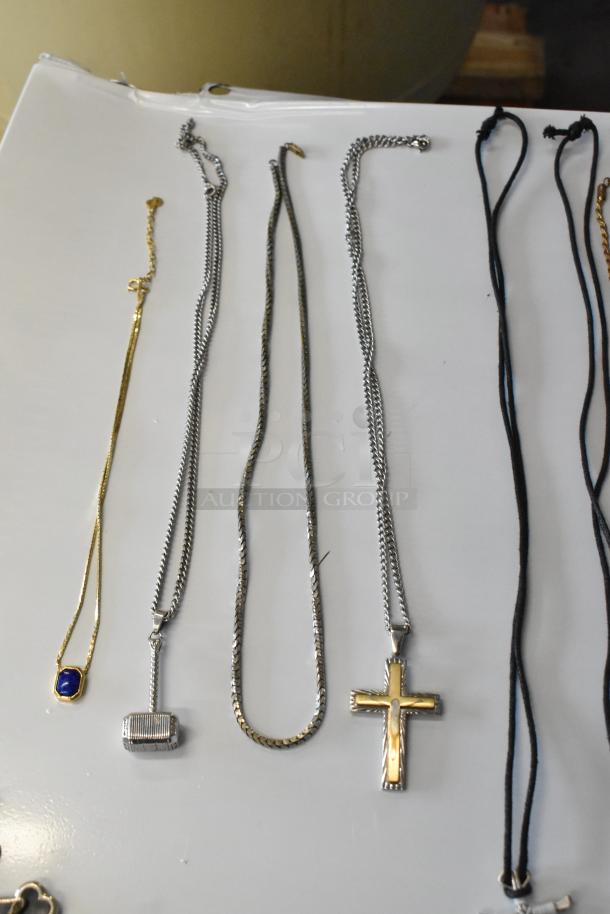 Lot of jewelry including various necklaces with pendants, in silver and gold tones, featuring a cross and a hammered texture.