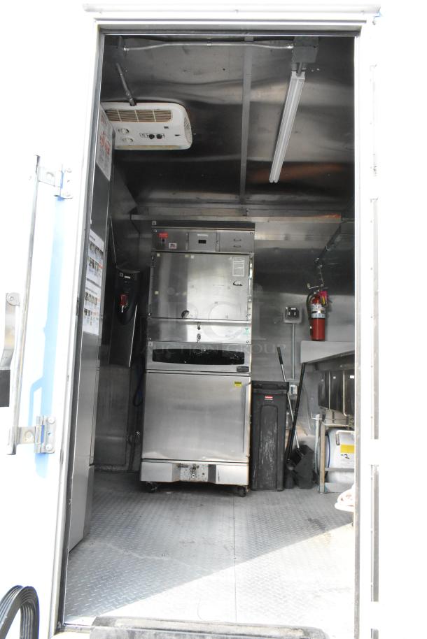 Fully equipped food trailer interior with stainless steel appliances, storage, lighting, and fire extinguisher, ready for use.