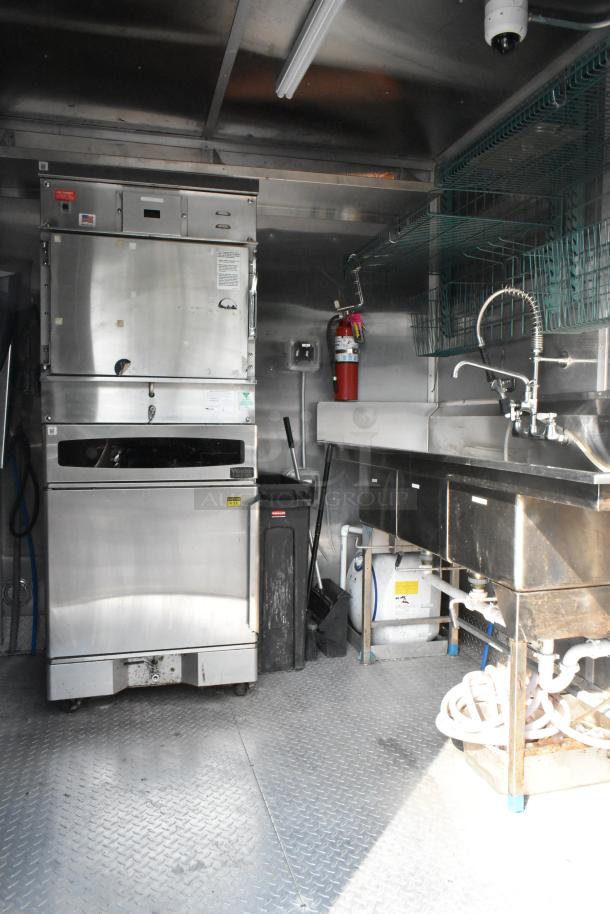Fully outfitted food trailer interior with stainless steel appliances, three-compartment sink, and fire extinguisher, ready for use.